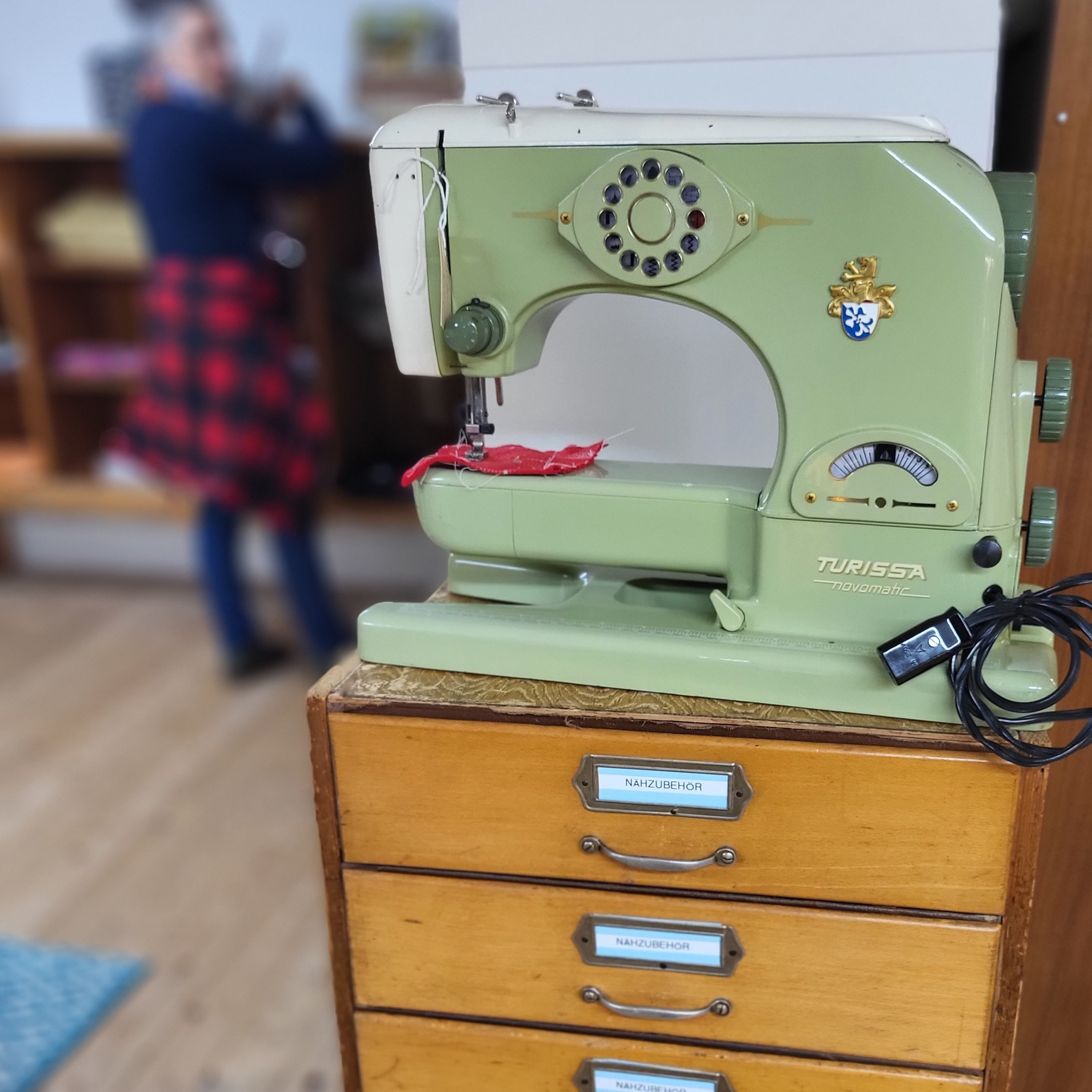 Hellgrüne Vintage-Nähmaschine der Marke Turissa Novomatic auf einer Holzkommode mit Schubladen für Nähzubehör.